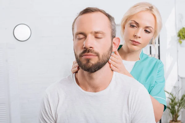 Retrato de fisioterapeuta masajeando cuello de hombre en clínica - foto de stock