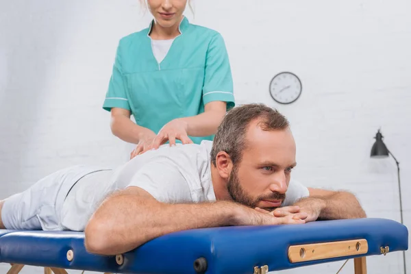 Частичный взгляд на женского массажиста, делающего массаж пациентке на массажном столе в клинике — стоковое фото