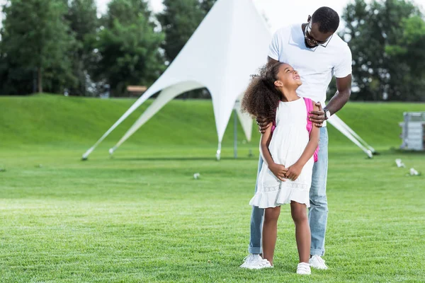 Afrikanisch-amerikanischer Vater umarmt Tochter mit Schultasche im Park — Stockfoto