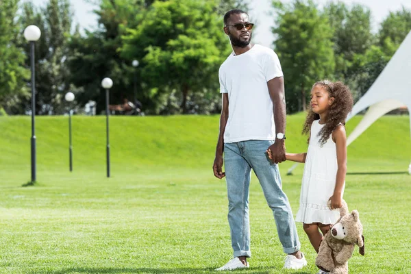 Afro-americanos padre e hija tomados de la mano y caminando en parque - foto de stock