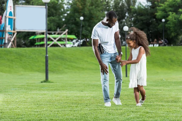 Afrikanisch-amerikanischer Polizist mit Waffe und Tochter an Händen und Fuß im Park — Stockfoto