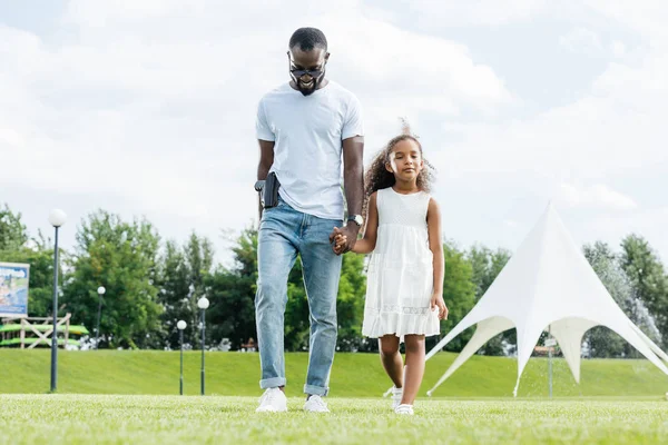 Afrikanisch-amerikanischer Polizist mit Pistole und Tochter an Händen und Fuß in Freizeitpark — Stockfoto