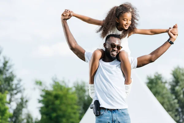 Poliziotto afroamericano con pistola che tiene la figlia sulle spalle nel parco divertimenti — Foto stock