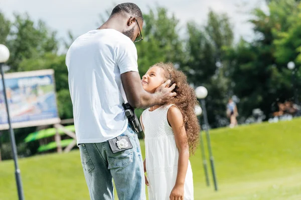 Afrikanisch-amerikanischer Polizist und Tochter umarmen und schauen einander im Freizeitpark an — Stockfoto