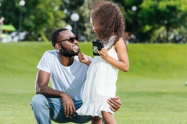Африканская американская дочь стоит с полицейским значком и трогает бороду отца в парке — стоковое фото