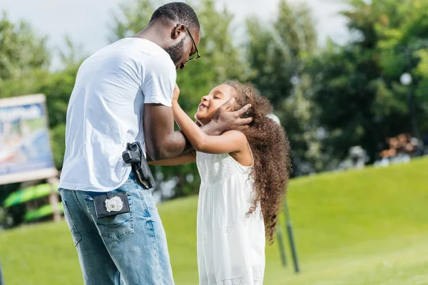 Policía afroamericana y su hija abrazándose en el parque de atracciones - foto de stock