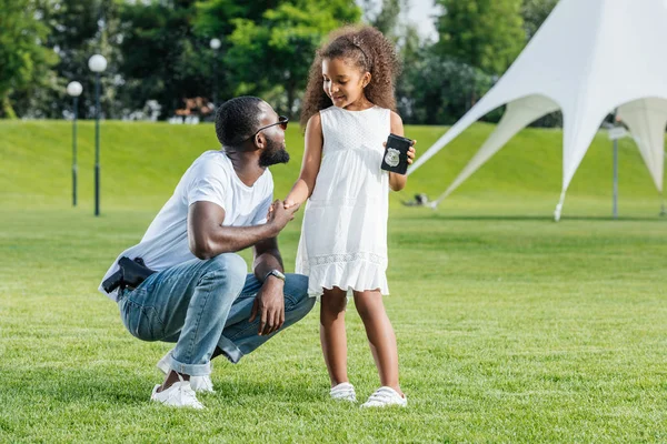 Afroamericana hija sosteniendo padre policía insignia en parque - foto de stock