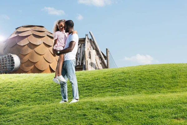 Afro-americano pai segurando filha na colina no parque de diversões — Fotografia de Stock