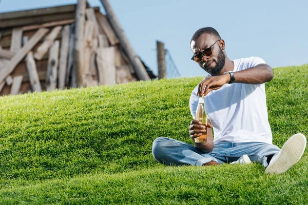 Bell'uomo afroamericano che apre una bottiglia di soda sulla collina verde — Foto stock