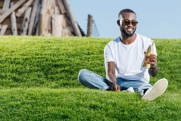 Schöner afrikanisch-amerikanischer Mann sitzt mit Soda auf grünem Hügel — Stockfoto