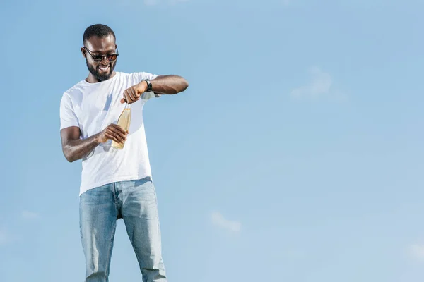 Happy handsome african american man opening soda bottle against blue sky — Stock Photo