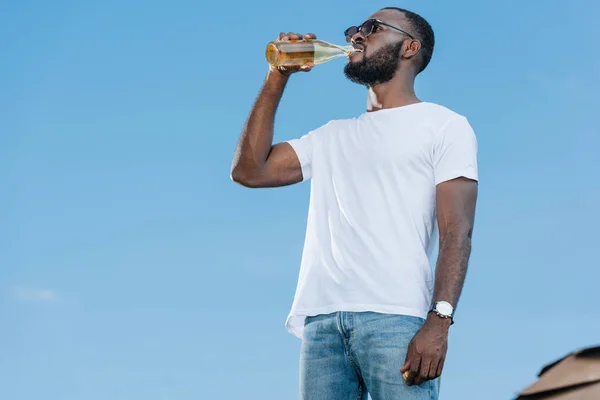 Homem americano africano bonito em óculos de sol bebendo refrigerante contra o céu azul — Fotografia de Stock