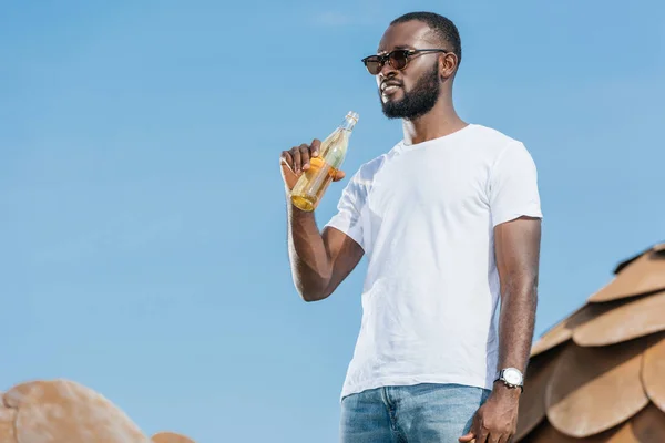 Handsome african american man drinking soda against blue sky — Stock Photo