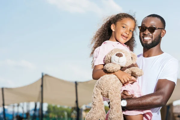 Lächelnd afrikanisch-amerikanischer Vater hält Tochter und sie schauen in die Kamera — Stockfoto