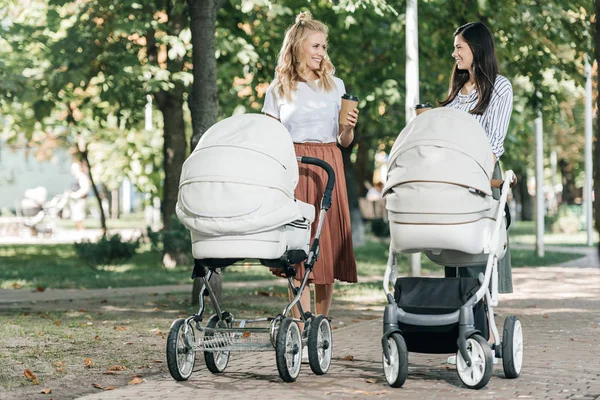 Матери держат кофе, чтобы пойти и ходить с детскими колясками в парке — стоковое фото