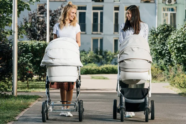 Матери, гуляющие с детскими колясками на улице и глядя друг на друга — стоковое фото