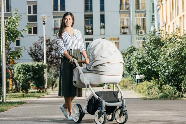 Mère debout dans la rue avec poussette bébé et regardant loin — Photo de stock