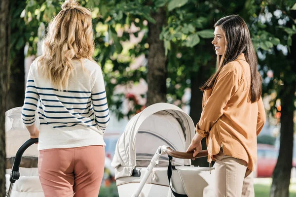 Back view of mothers walking with baby strollers in park and looking at each other — Stock Photo
