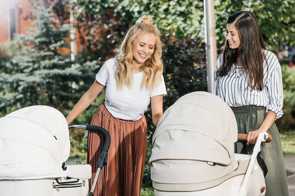Smiling mothers looking at baby strollers in park — Stock Photo
