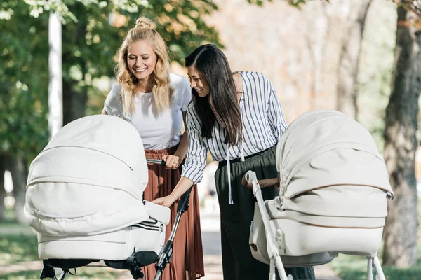 Улыбающиеся матери, смотрящие в детскую коляску в парке — стоковое фото