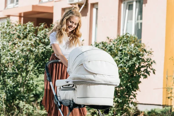 Attraktive, glückliche Mutter mit Blick auf Kinderwagen auf der Straße — Stockfoto