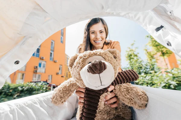 Smiling mother holding teddy bear in baby stroller — Stock Photo