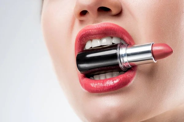 Cropped view of woman holding pink lipstick in teeth,  isolated on white — Stock Photo