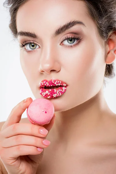 Attraktive Frau mit Zuckerstreuern auf den Lippen, die rosa Macaron hält, isoliert auf weiß — Stockfoto