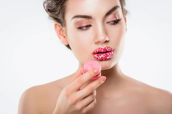 Приваблива дівчина з цукровими зморшками на губах тримає рожевий макарон, ізольована на білому — стокове фото