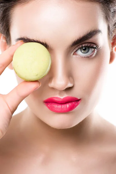 Mulher atraente segurando macaron verde na frente do olho, isolado em branco — Fotografia de Stock