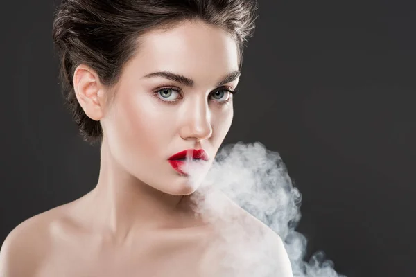 Красивая модная женщина, дующая в дым, изолированная на сером — стоковое фото