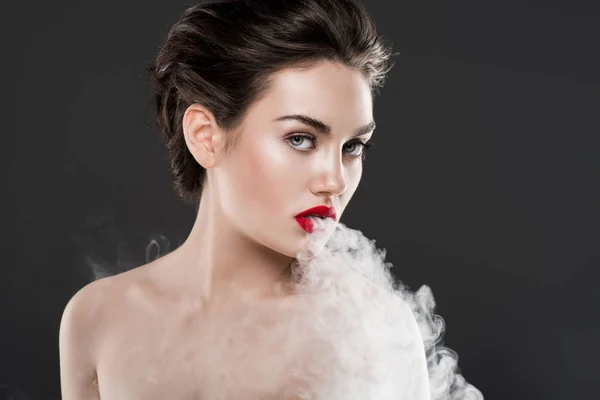 Hermosa mujer desnuda vapeando y soplando humo, aislado en gris - foto de stock