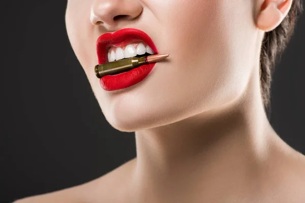 Vista recortada de mujer agresiva sosteniendo bala en los dientes, aislado en gris - foto de stock