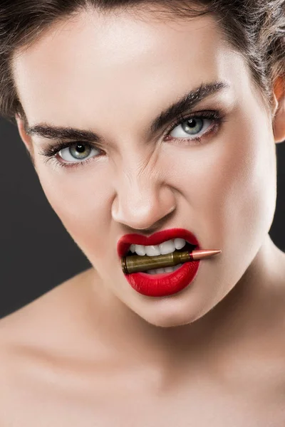 Atractiva mujer enojada sosteniendo bala en los dientes, aislado en gris - foto de stock