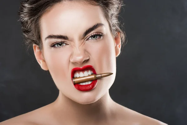 Mujer elegante agresiva sosteniendo bala en los dientes, aislado en gris - foto de stock
