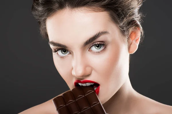 Attraente donna mordere barretta di cioccolato, isolato su grigio — Foto stock