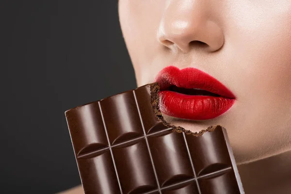 Vista ritagliata di donna con labbra rosse mangiare barretta di cioccolato, isolato su grigio — Foto stock