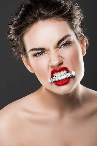Сердитая красивая женщина с долларовой купюрой в зубах, изолированная от серого — стоковое фото