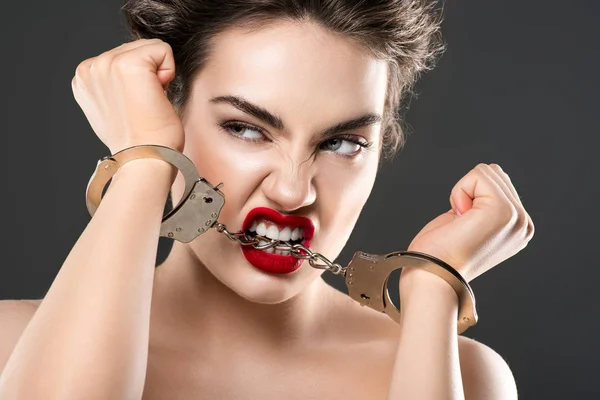 Attractive sensual girl biting handcuffs, isolated on grey — Stock Photo