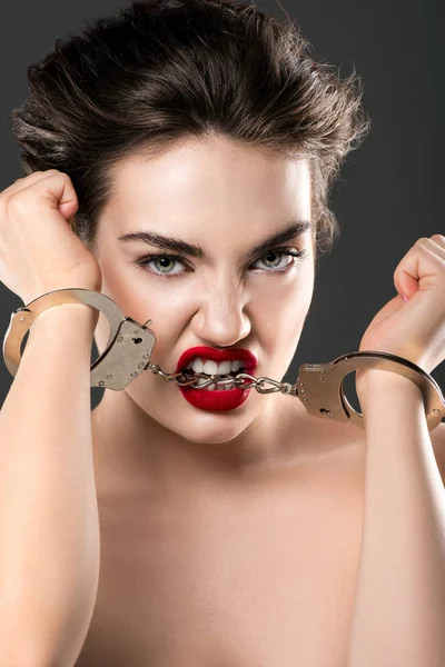 Young passionate woman biting handcuffs, isolated on grey — Stock Photo