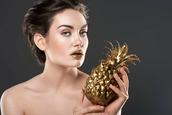 Attractive naked woman with golden makeup holding pineapple, isolated on grey — Stock Photo