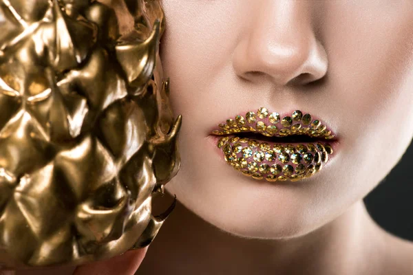 Cropped view of woman with gild lips holding golden pineapple — Stock Photo