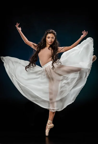 Young female ballet dancer in white skirt posing on dark backdrop — Stock Photo