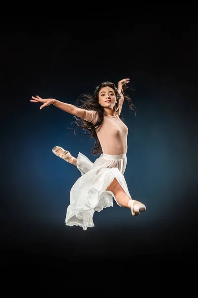Молода балерина в елегантному одязі стрибає на темному тлі — стокове фото