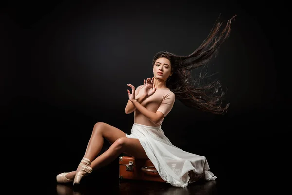 Beautiful ballerina in white skirt resting on retro suitcase on dark background — Stock Photo