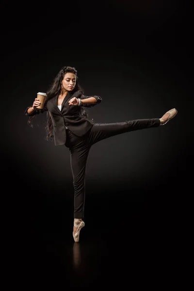 Привлекательная молодая деловая женщина в формальной одежде и балетной обуви с кофе, чтобы пойти проверить время на черном фоне — стоковое фото