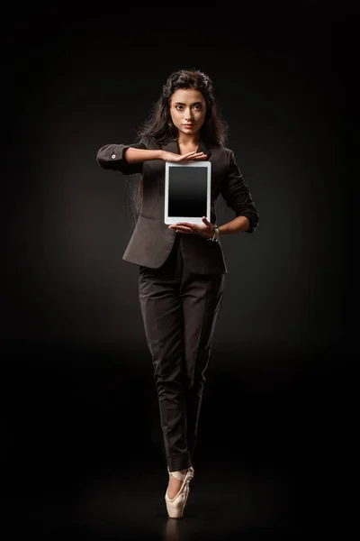 Attractive businesswoman in suit and ballet shoes showing tablet with blank screen on black backdrop — Stock Photo