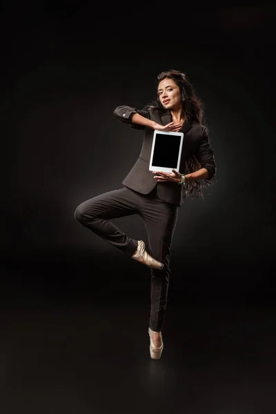 Hermosa mujer de negocios en traje y zapatos de ballet mostrando tableta con pantalla en blanco sobre fondo negro - foto de stock