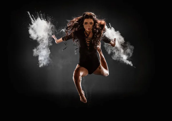 Hermosa bailarina en body negro con talco saltando sobre fondo oscuro - foto de stock