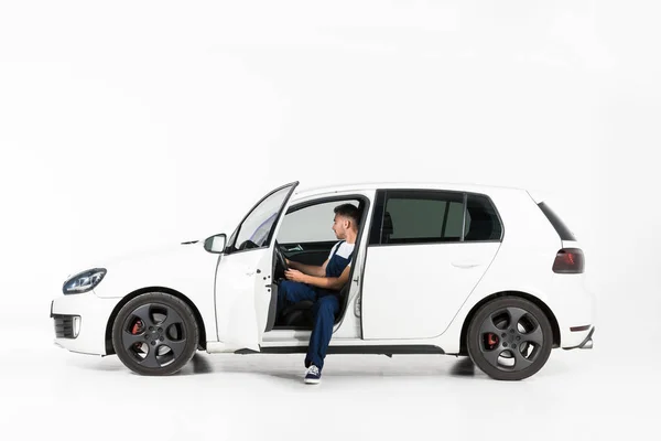 Vista lateral de mecánico auto guapo sentado en el coche en blanco - foto de stock